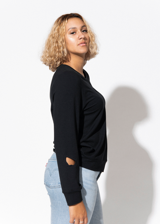 Person wearing a black sweater and light blue jeans against a white background
