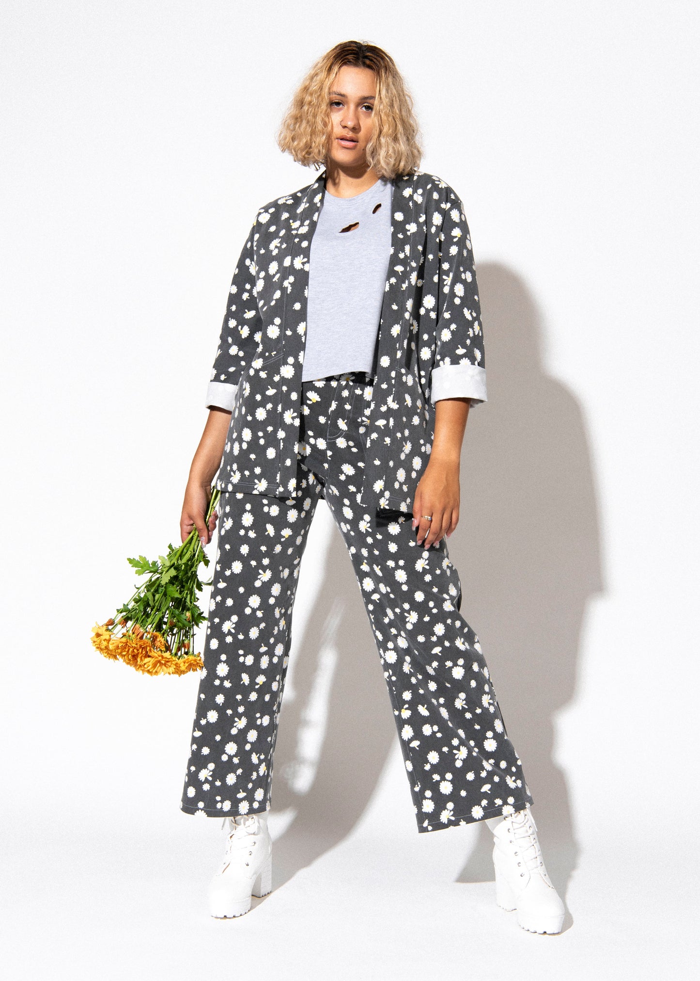 Person wearing a gray floral outfit holding flowers against a white background