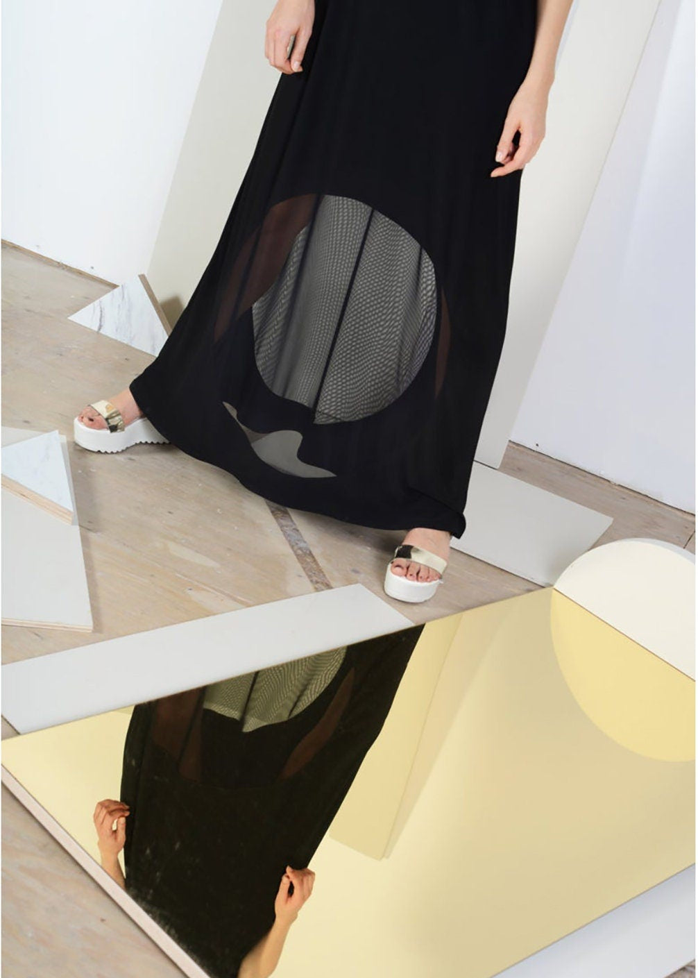 Person wearing a black dress with sheer panels standing on a reflective surface.