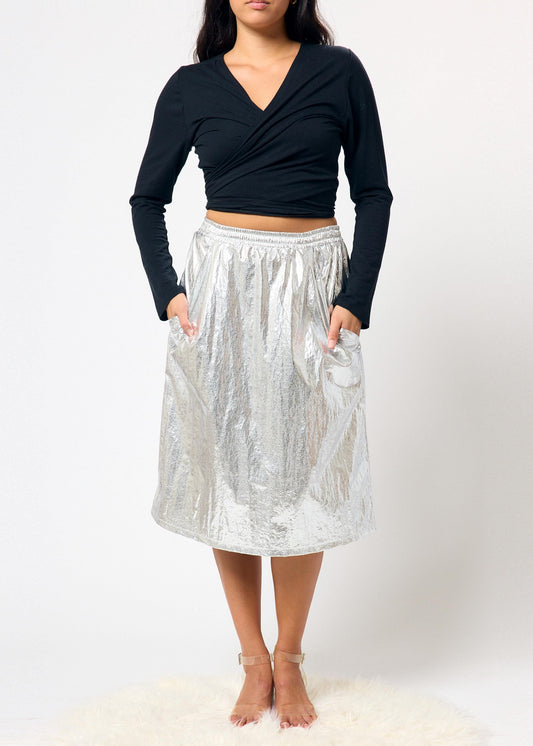 Person wearing a black long-sleeve top and silver metallic skirt on a white background