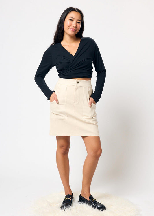 Woman wearing a black top and beige denim skirt against a white background