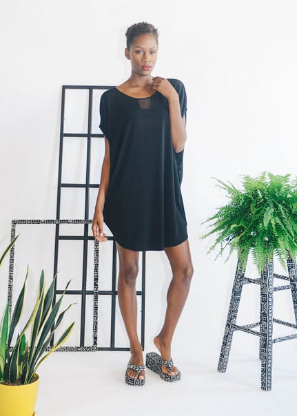 woman standing i room with windowpanes and plants, wearing a black dress