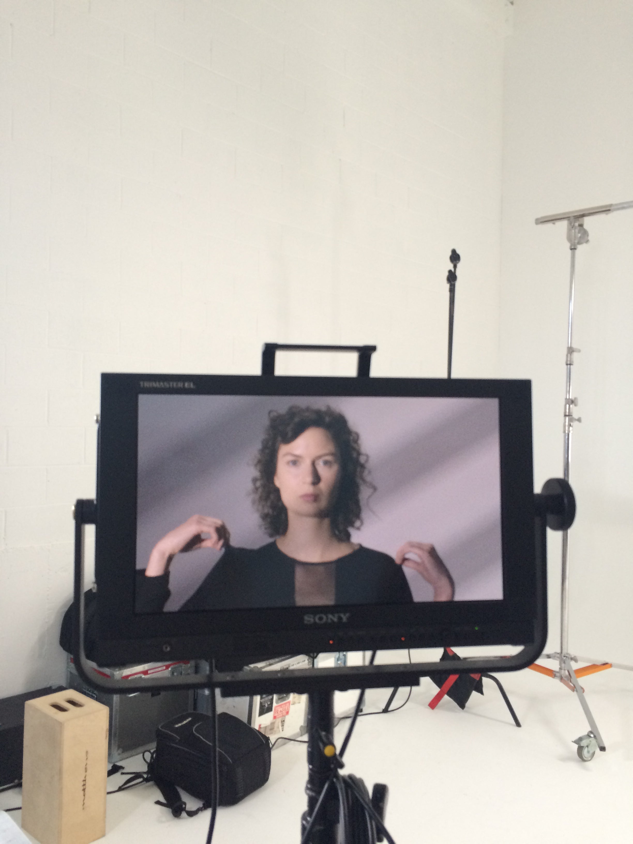 Monitor displaying a person with a blurred background on a stand with equipment around.