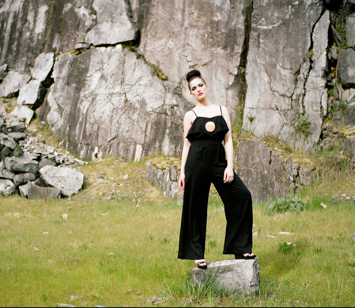 Person wearing a black outfit standing on a rock with a rocky cliff background