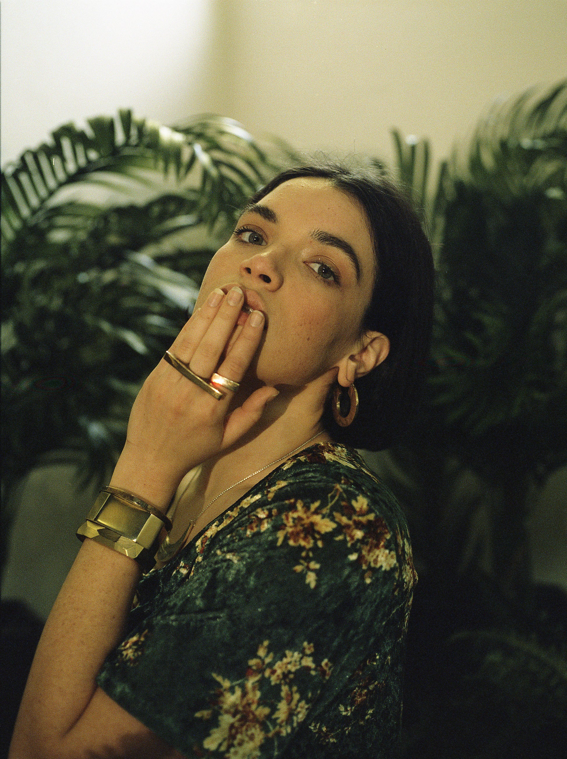 Woman with dark hair and floral dress sitting in a room with plants