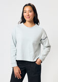 Woman wears cropped pale blue long sleeve t-shirt with black embroidered barbed wire design on left arm