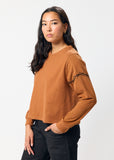Woman wearing a brown long-sleeve top with embroidered black barbed wire detail on sleeve on a white background