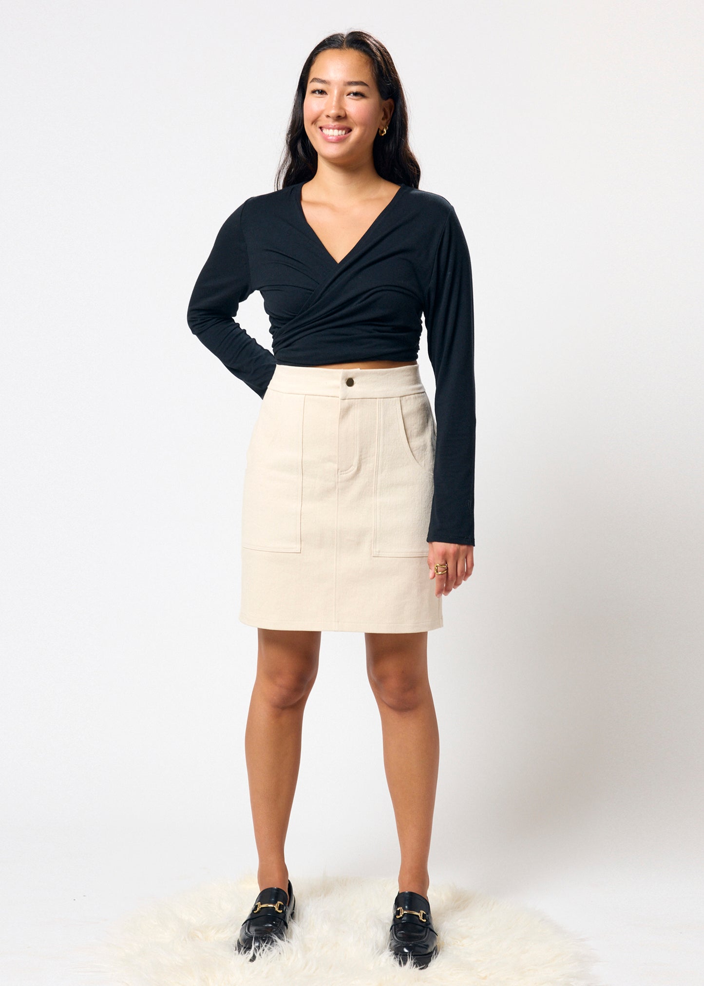 Woman wearing a black long-sleeve top and beige denim skirt on a white background