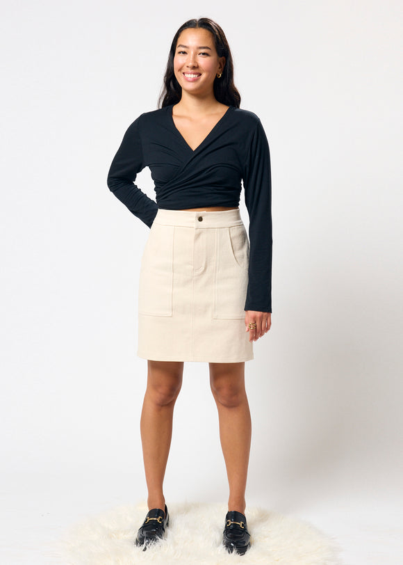 Woman wearing a black long-sleeve top and beige denim skirt on a white background