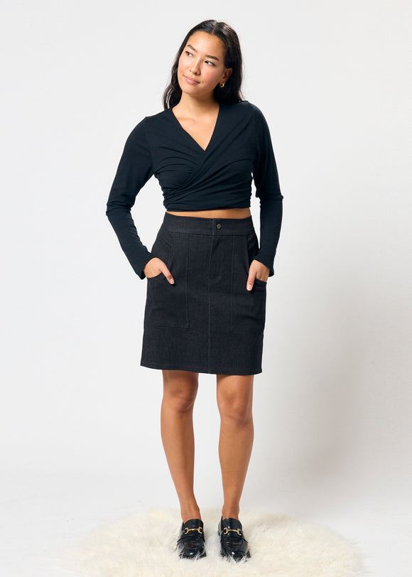 Woman wearing a black long-sleeve top and black denim skirt on a white background