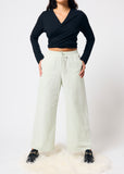 Person wearing a black top and pale green pants on a white background