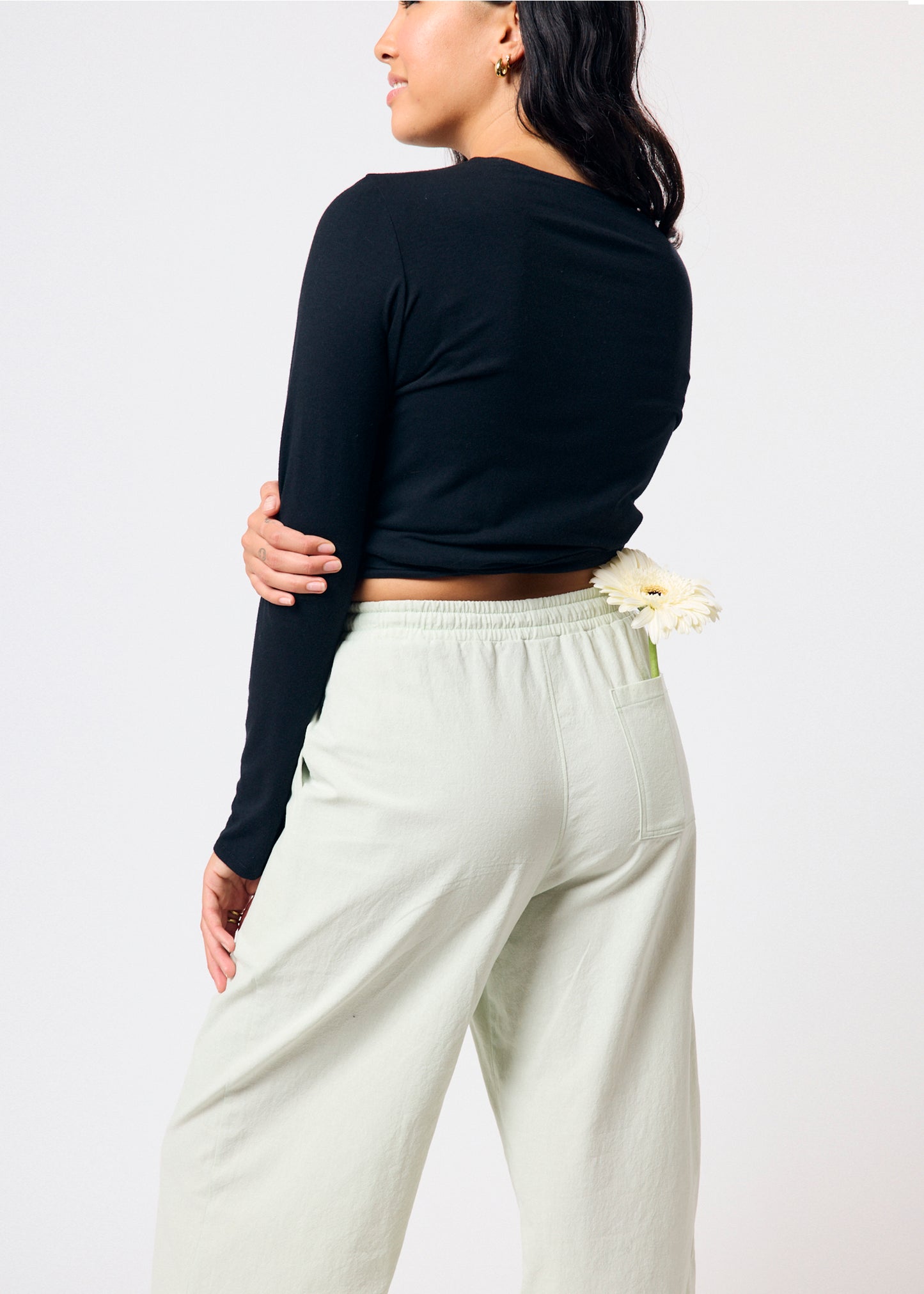 Person wearing a black long-sleeve top and pale green pants on a plain background