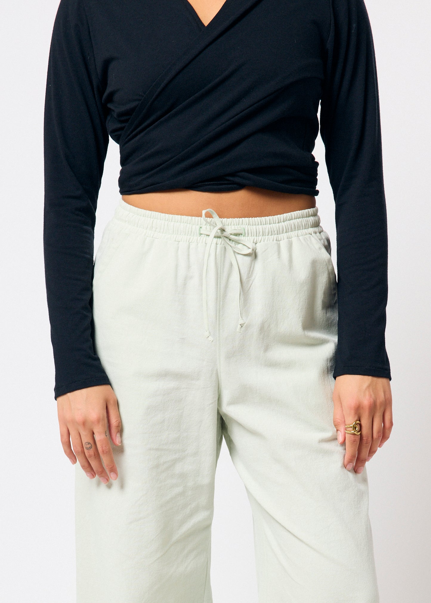 Person wearing a black long-sleeve top and pale green pants on a plain background