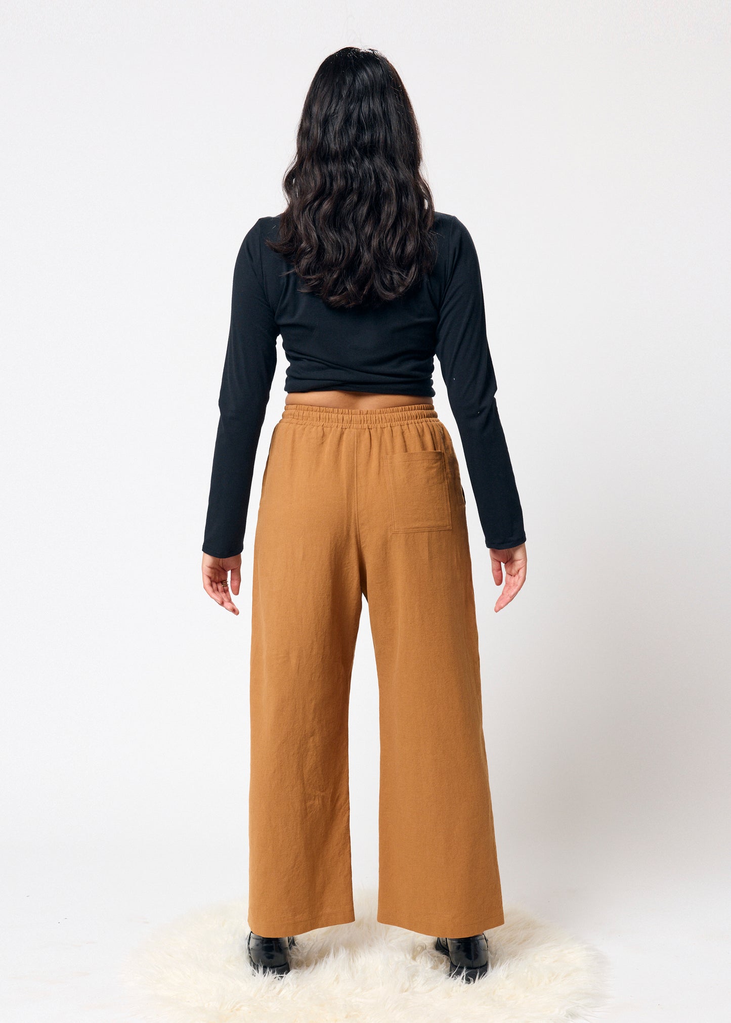 Person wearing a black long-sleeve top and tan wide-leg pants on a white background