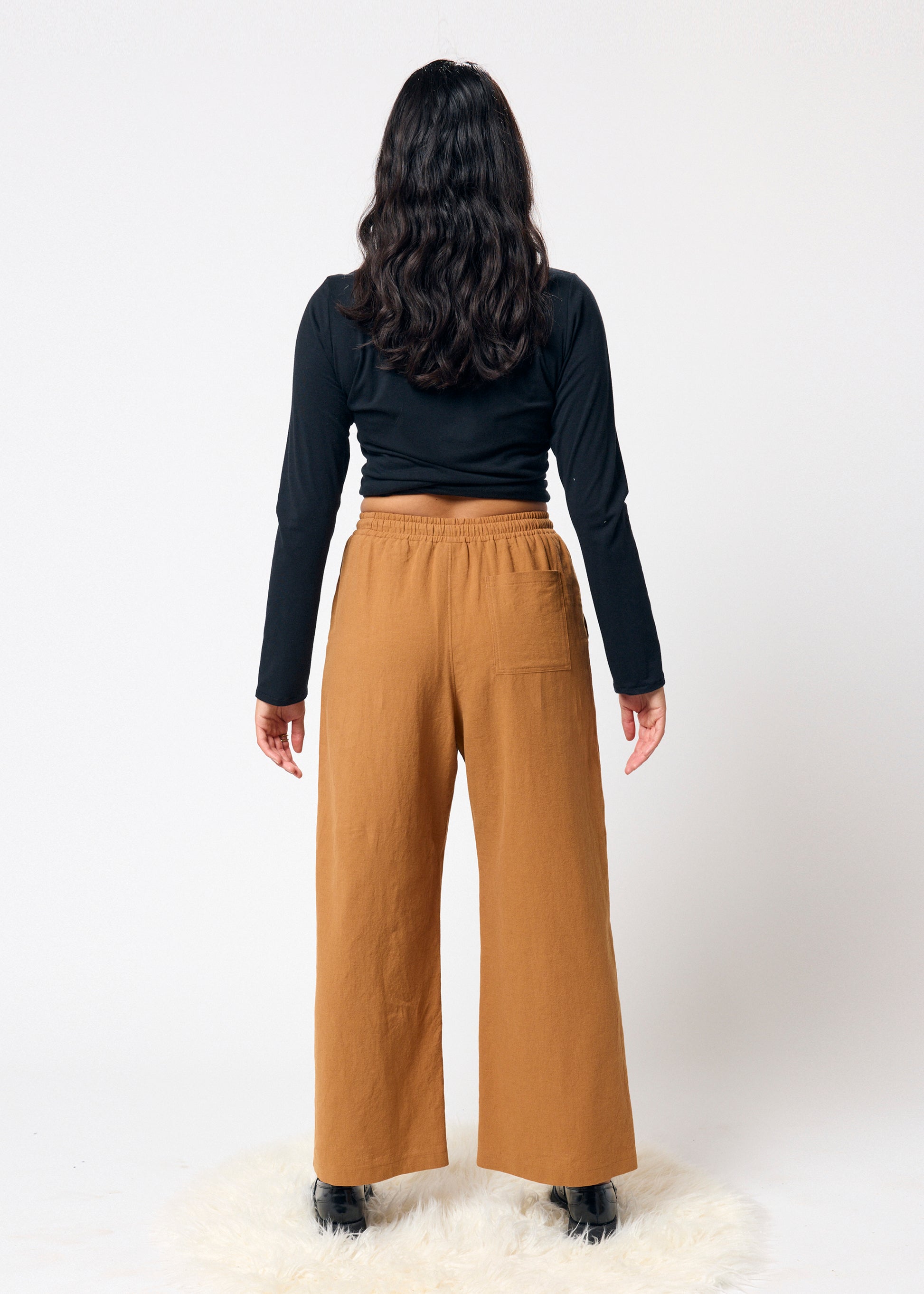 Person wearing a black long-sleeve top and tan wide-leg pants on a white background
