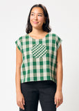 Woman wearing a green and white checkered top with a circle design on a plain background