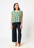Woman wearing a green and white checkered top and black pants on a white background