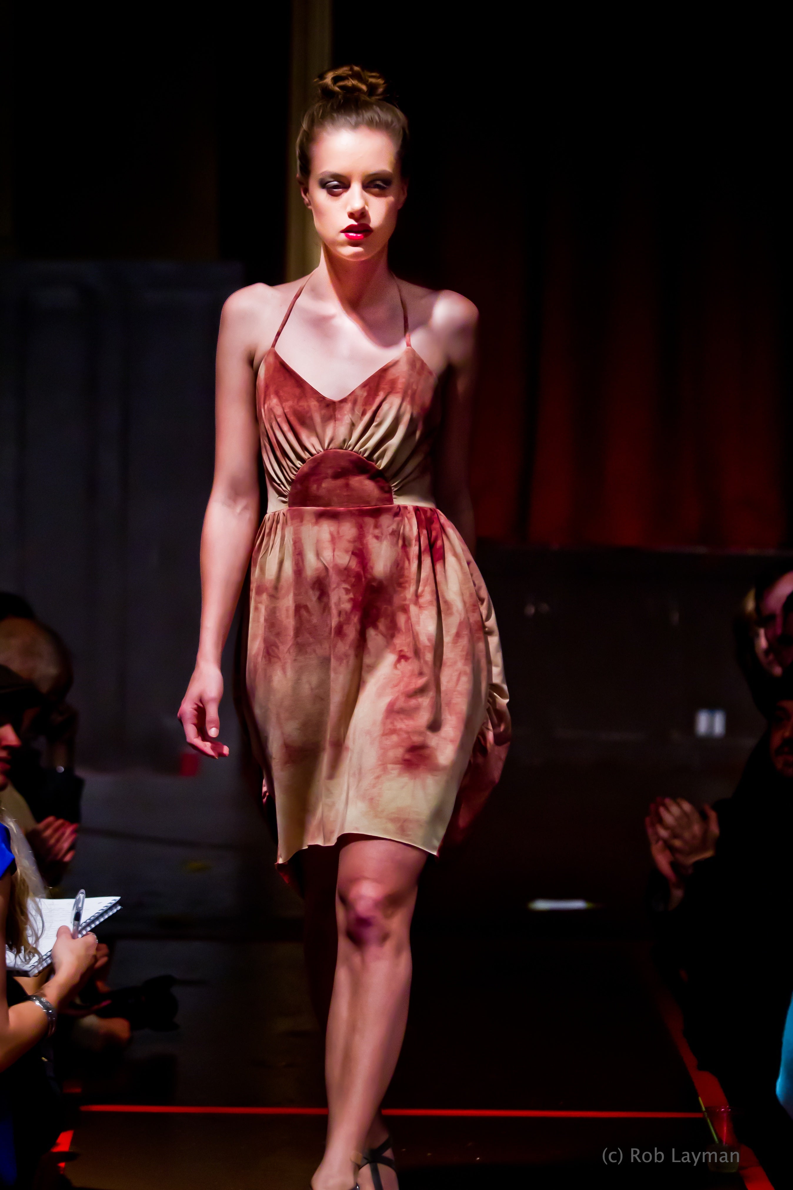 Model walking on a runway wearing a red and gold dress.