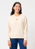 Woman wearing a beige sweatshirt with a heart cut out and blue pants against a white background