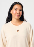 Woman wearing a beige sweater with a heart cutout design on a plain background