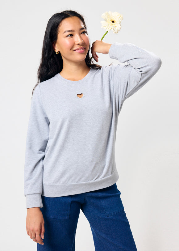 Woman wearing a light gray sweatshirt with a small heart cut out, holding a white flower against a plain background