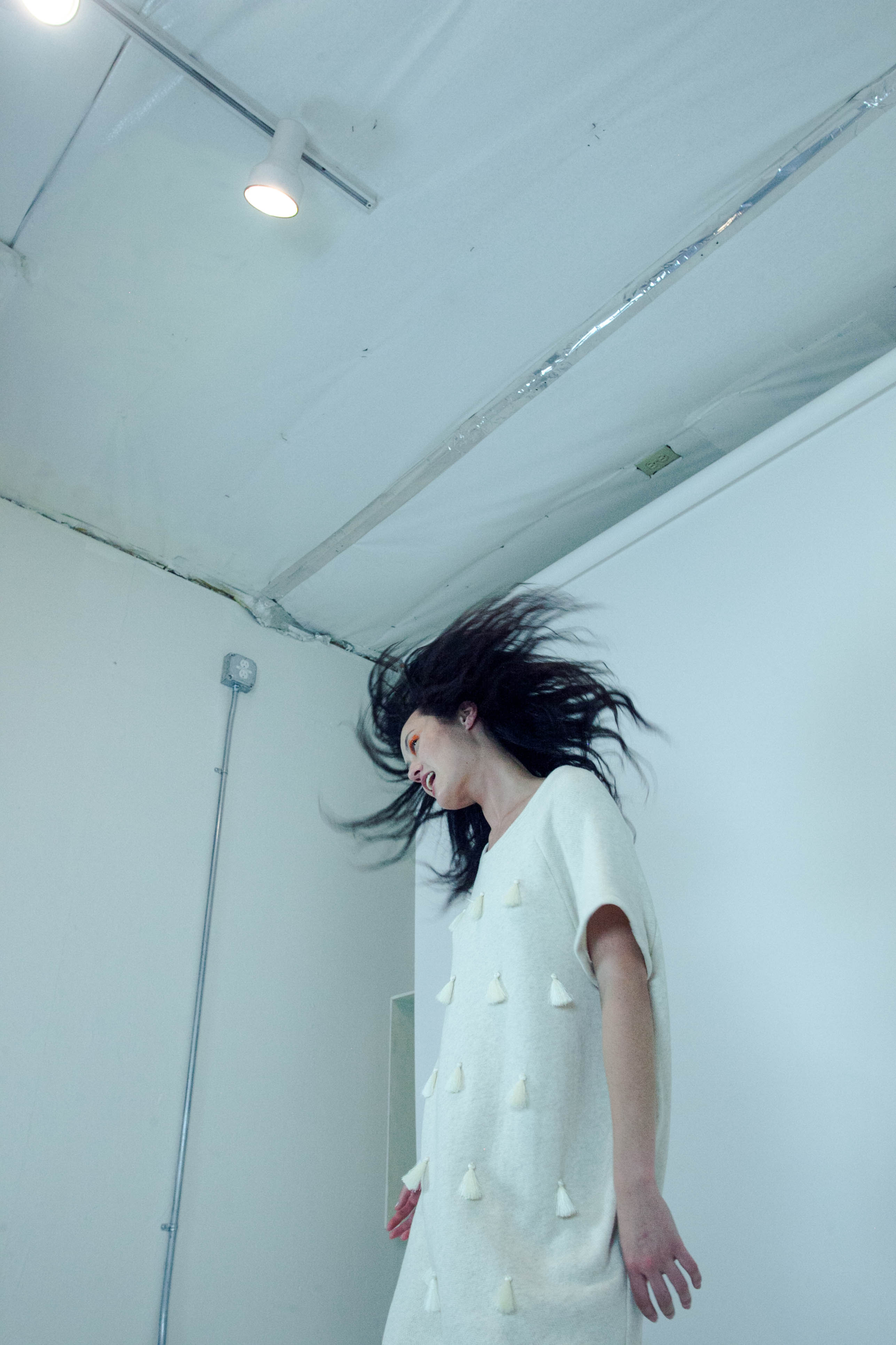 Woman in a white dress standing against a white wall with her hair blowing.