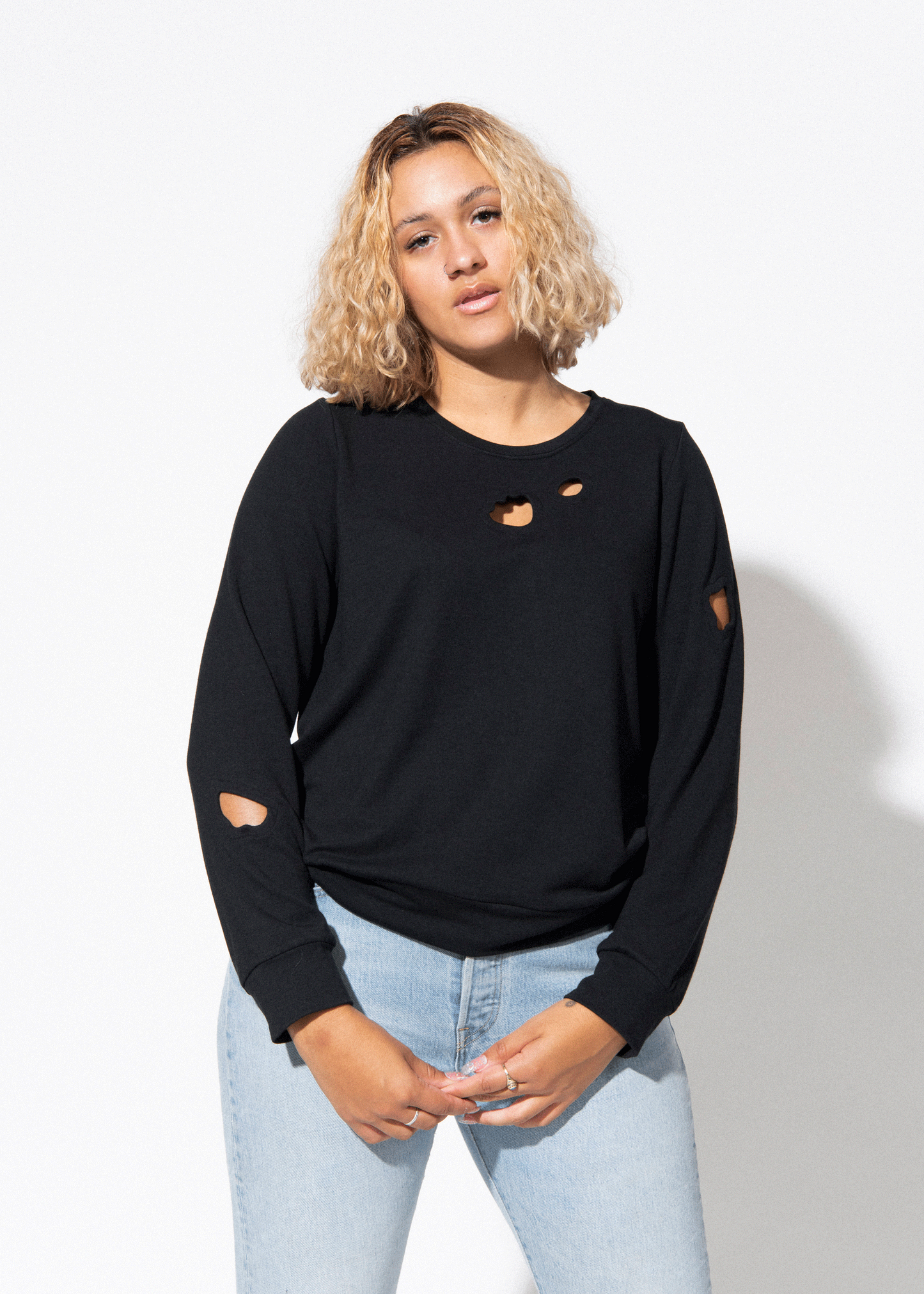 Woman wearing a black oversized sweater with heart cutouts and light blue jeans on a white background