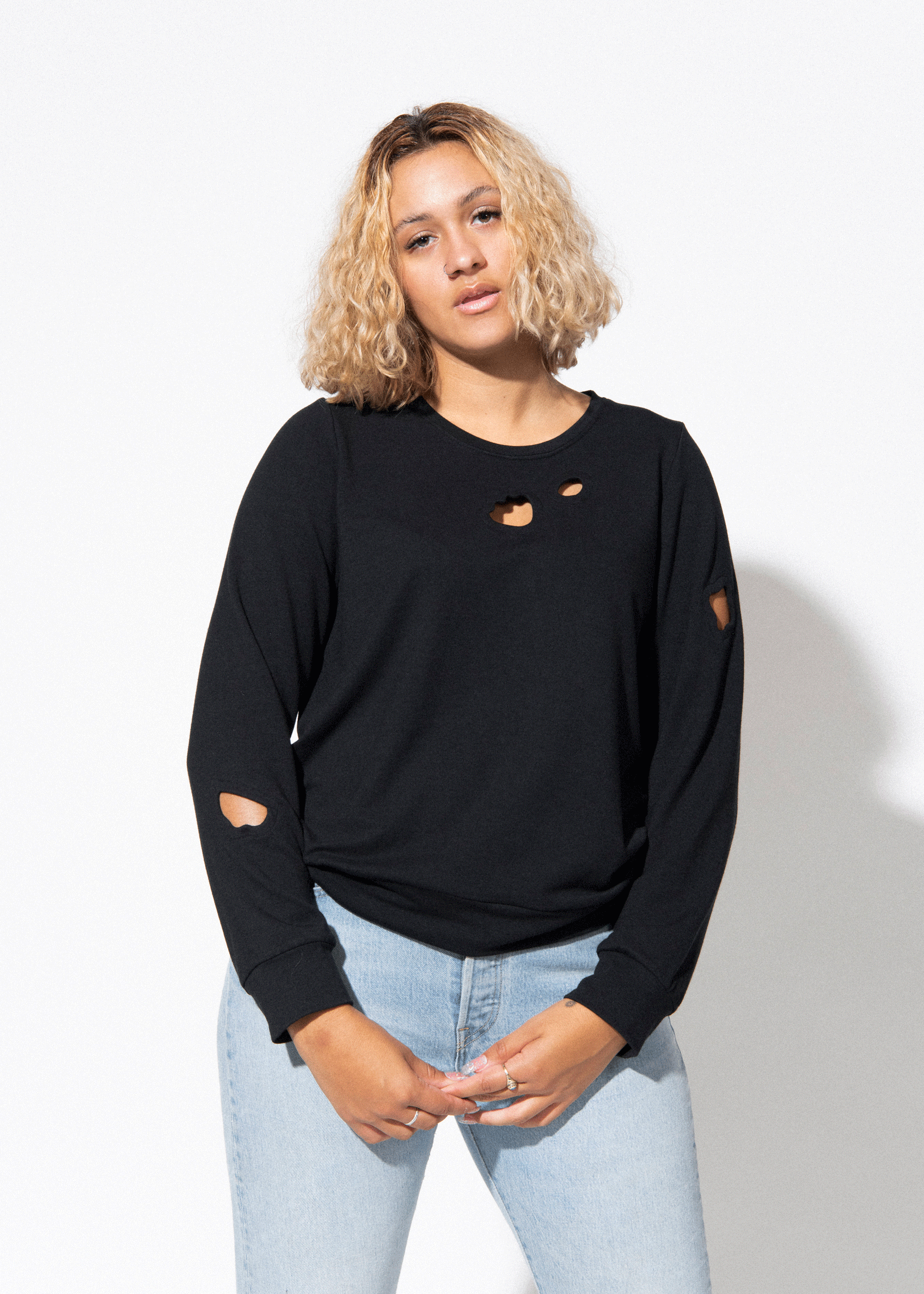 Woman wearing a black oversized sweater with heart cutouts and light blue jeans on a white background