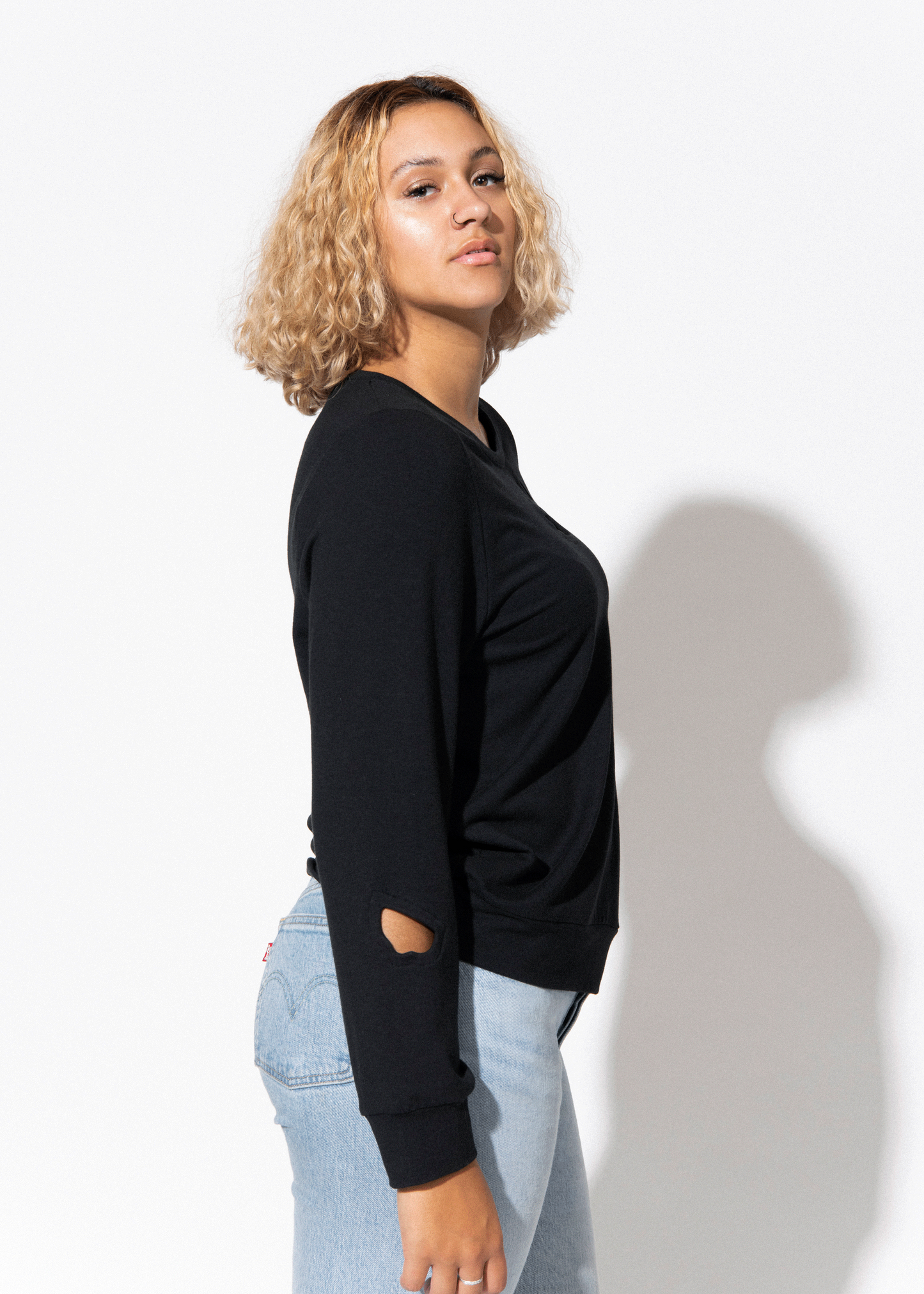 Person wearing a black sweater and light blue jeans against a white background