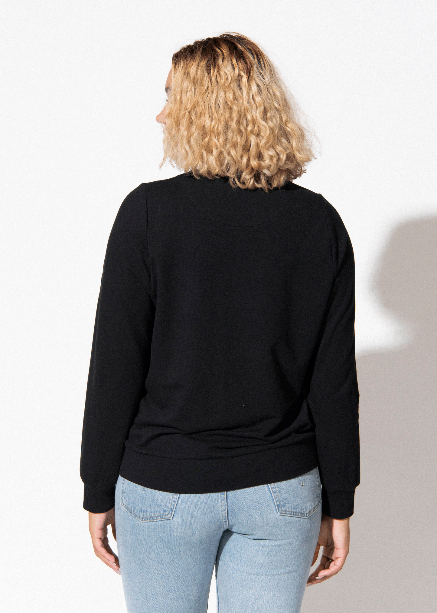 Person wearing a black long-sleeve top and light blue jeans on a white background