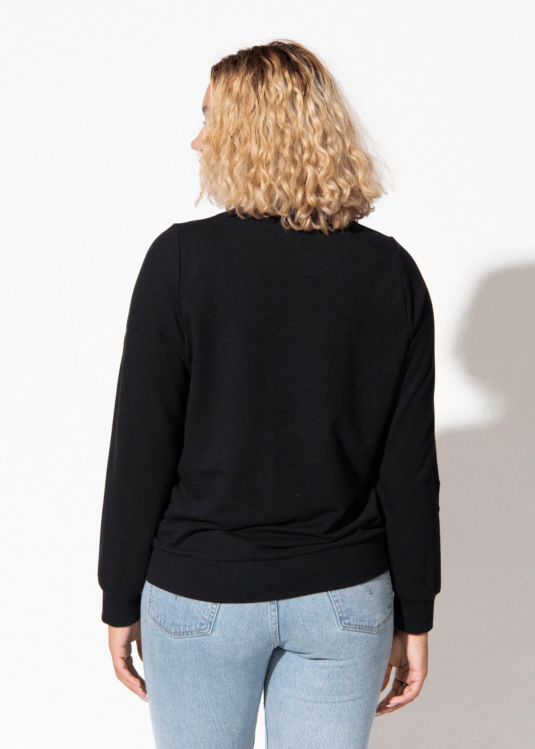 Person wearing a black long-sleeve top and light blue jeans on a white background