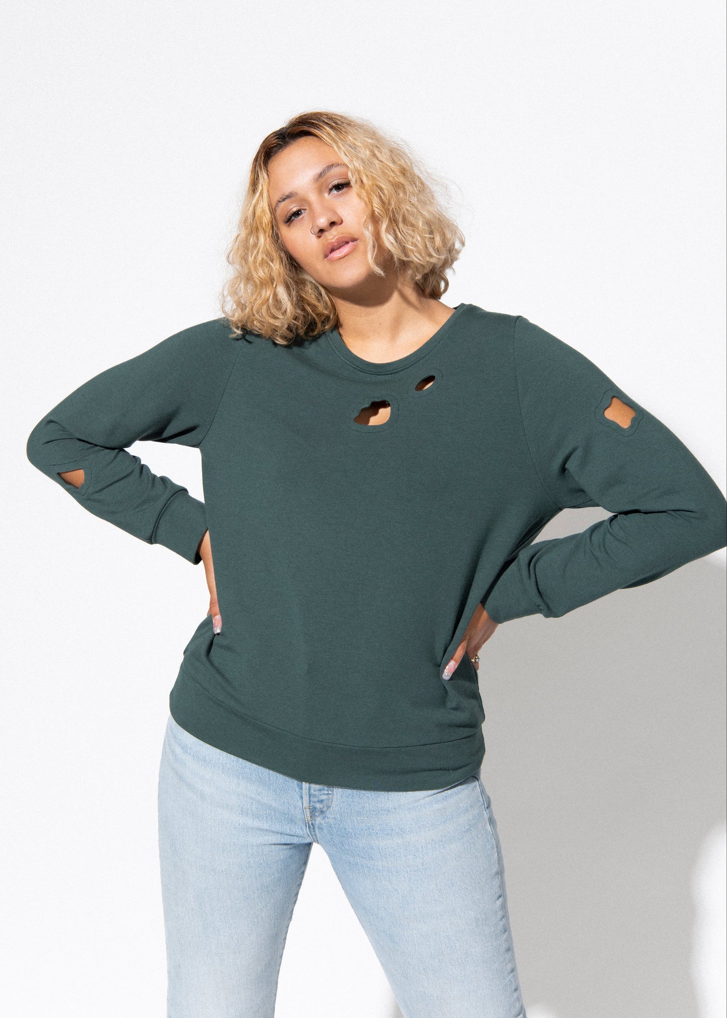 Woman wearing a green distressed sweatshirt and light blue jeans on a white background
