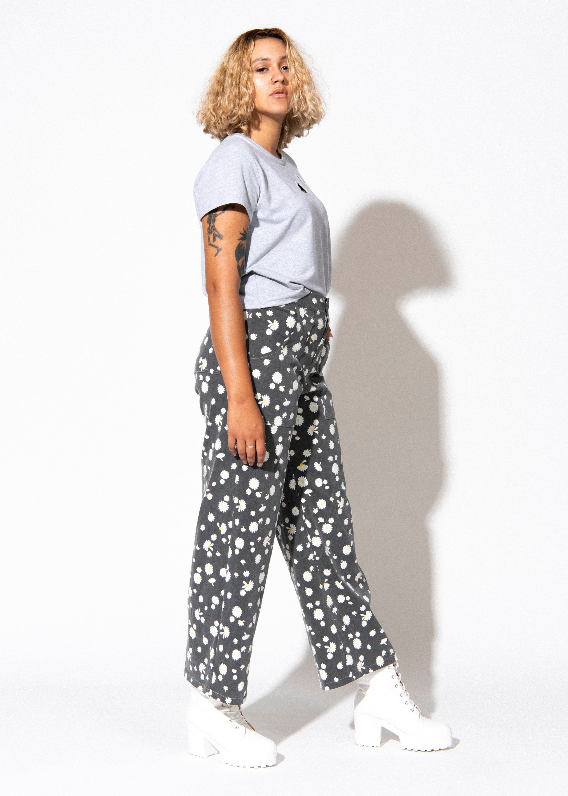 Person wearing a light blue t-shirt and patterned pants standing against a white background