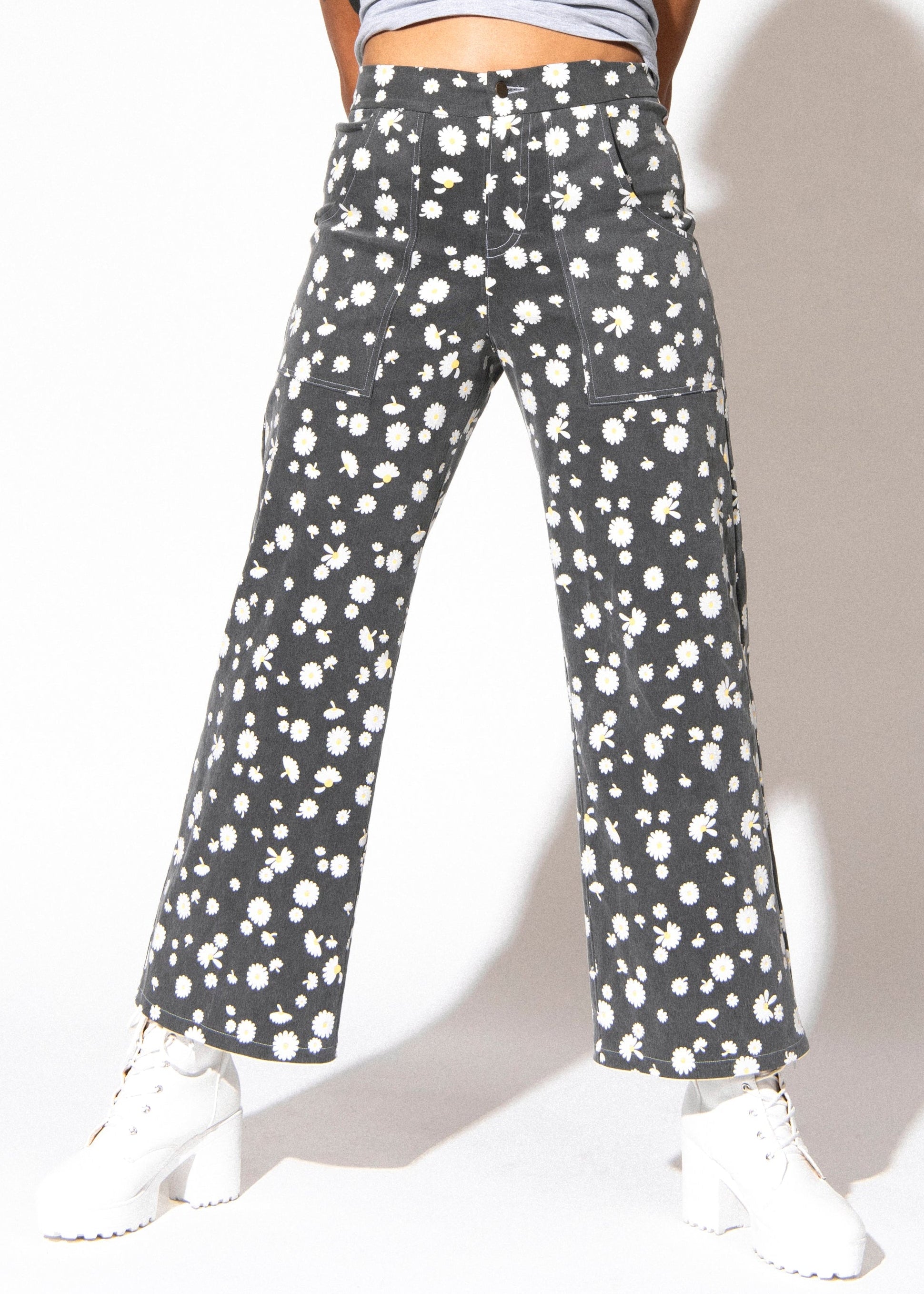Person wearing gray pants with white floral pattern on a plain background