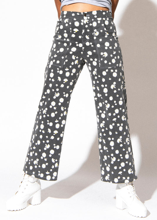 Person wearing gray pants with white floral pattern on a plain background