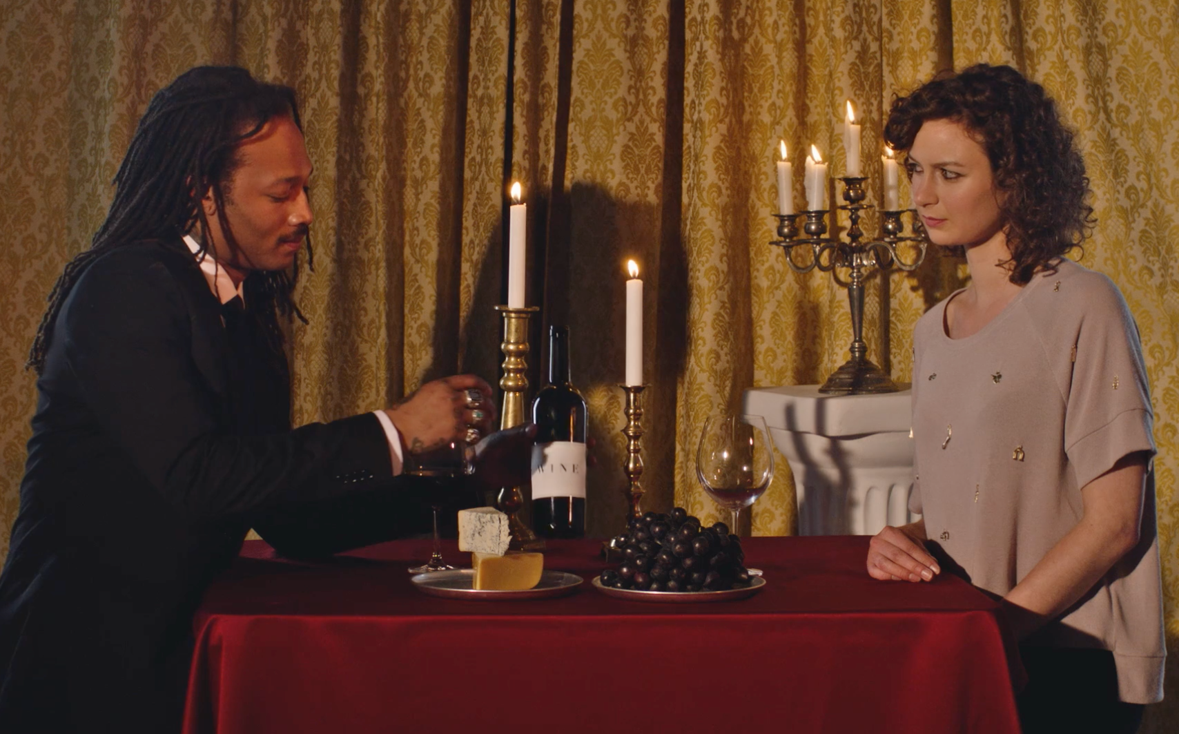 Two people sitting at a table with wine and food, surrounded by candles and a chandelier.