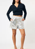Person wearing a black long-sleeve top and silver metallic shorts on a white background