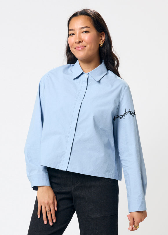 Woman wearing a light blue shirt with black embroidery on a white background