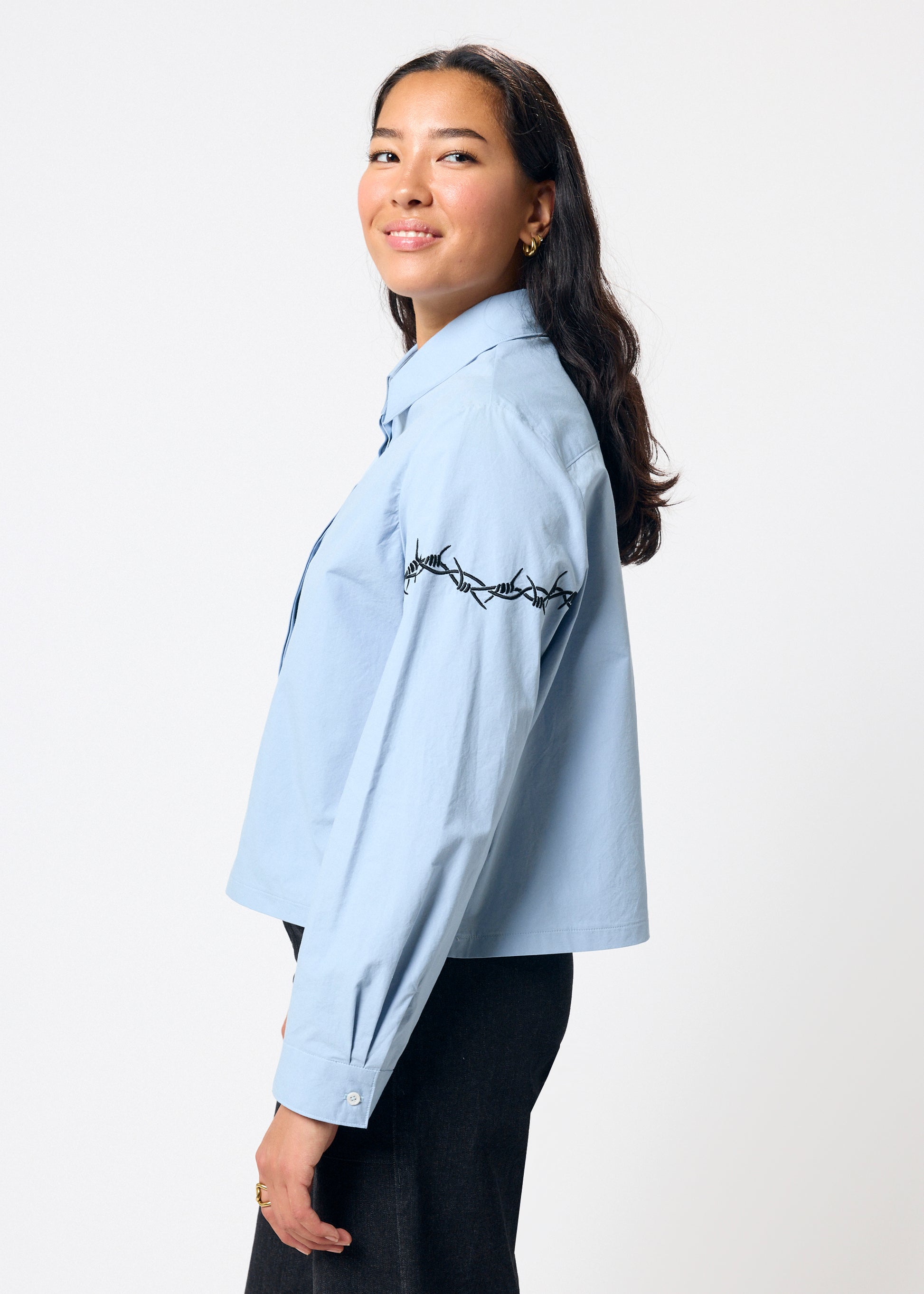 Woman wearing a light blue shirt with embroidery on a white background