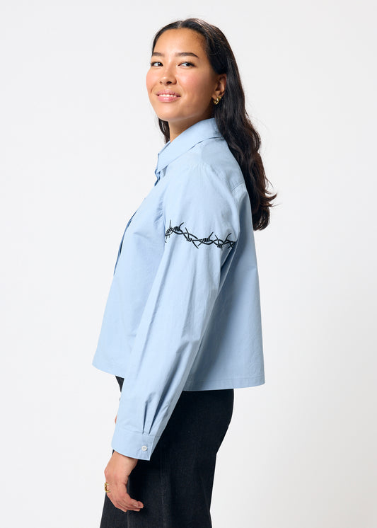 Woman wearing a light blue shirt with embroidery on a white background