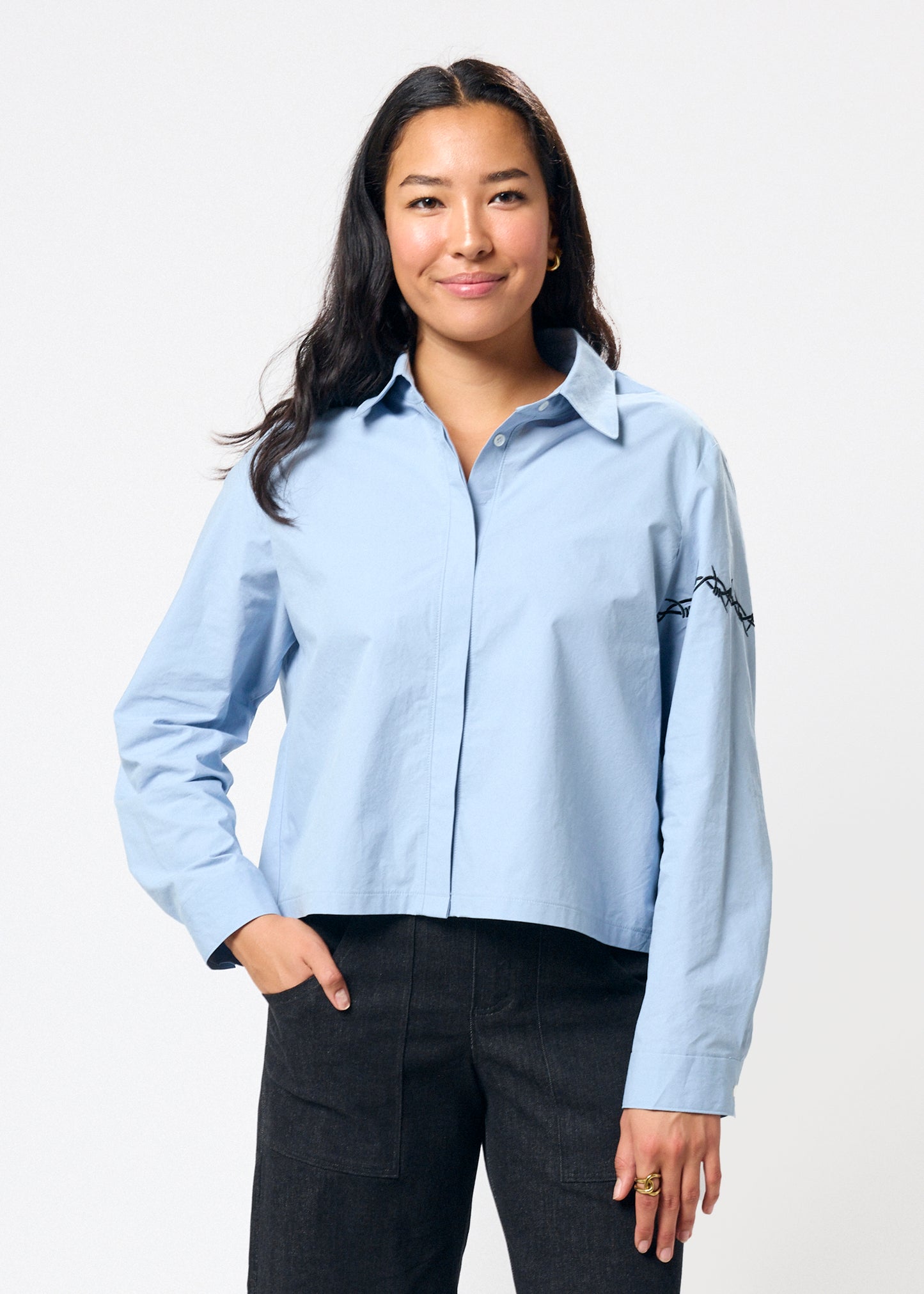 Woman wearing a light blue shirt with black embroidery on a white background