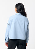 Person wearing a light blue shirt with black embroidery on the sleeve against a white background