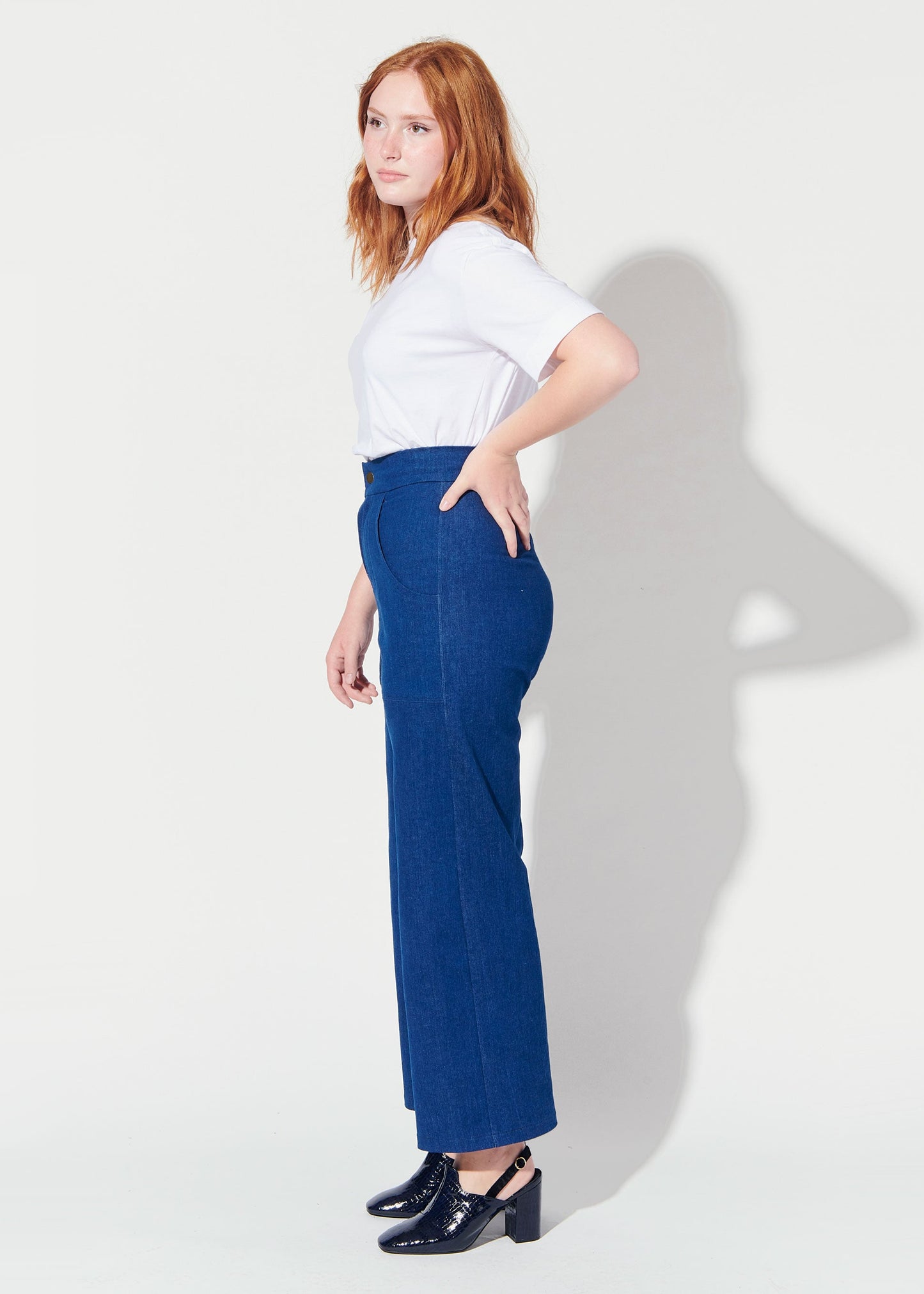 Woman wearing a white top and blue pants against a white background