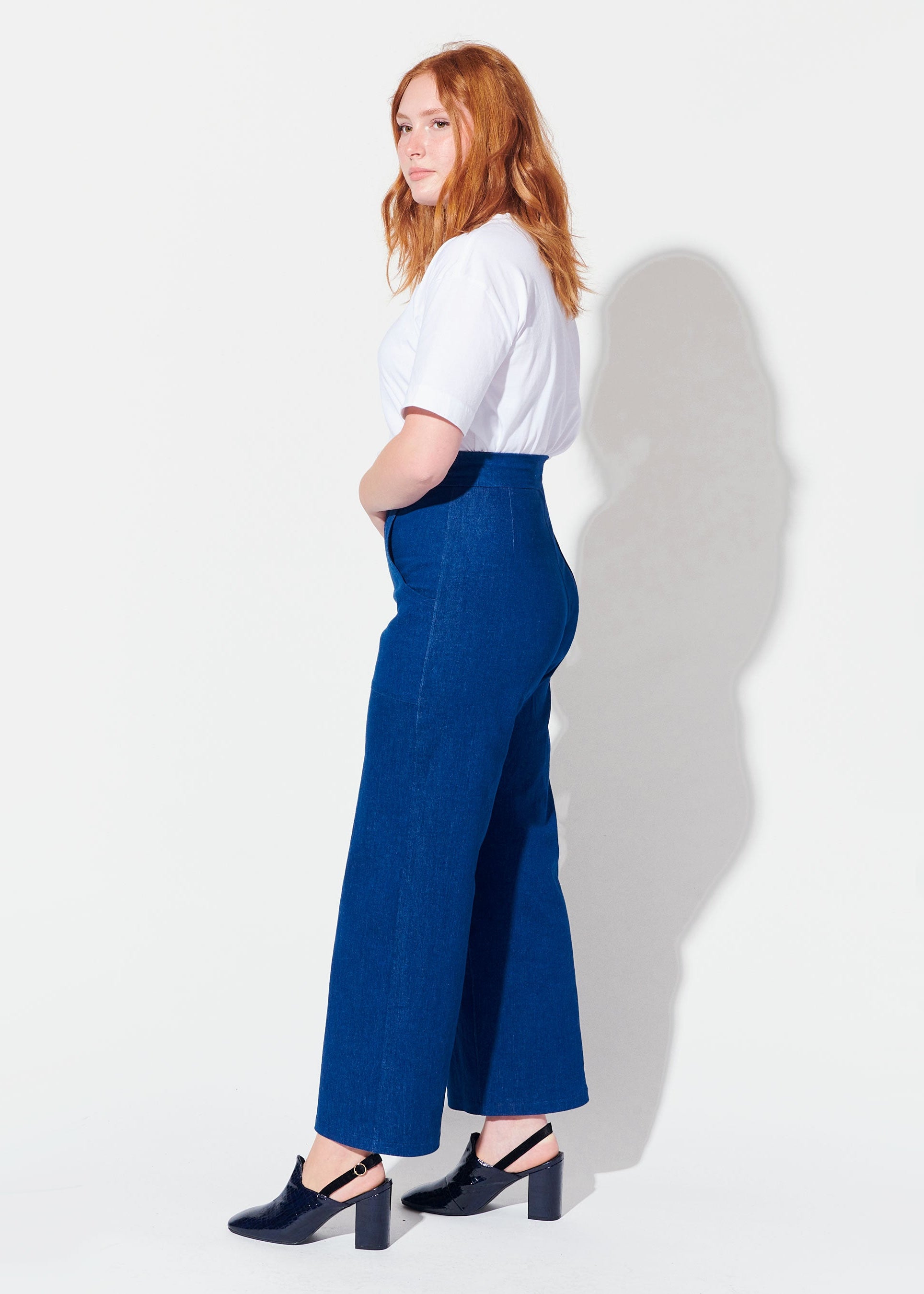 Woman wearing a white top and blue pants against a white background