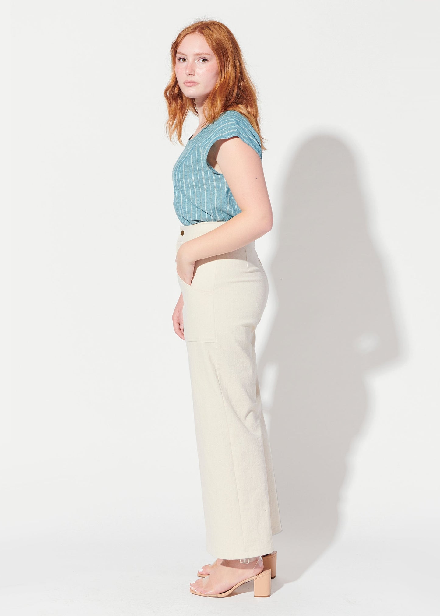 Woman wearing a blue top and white pants against a white background