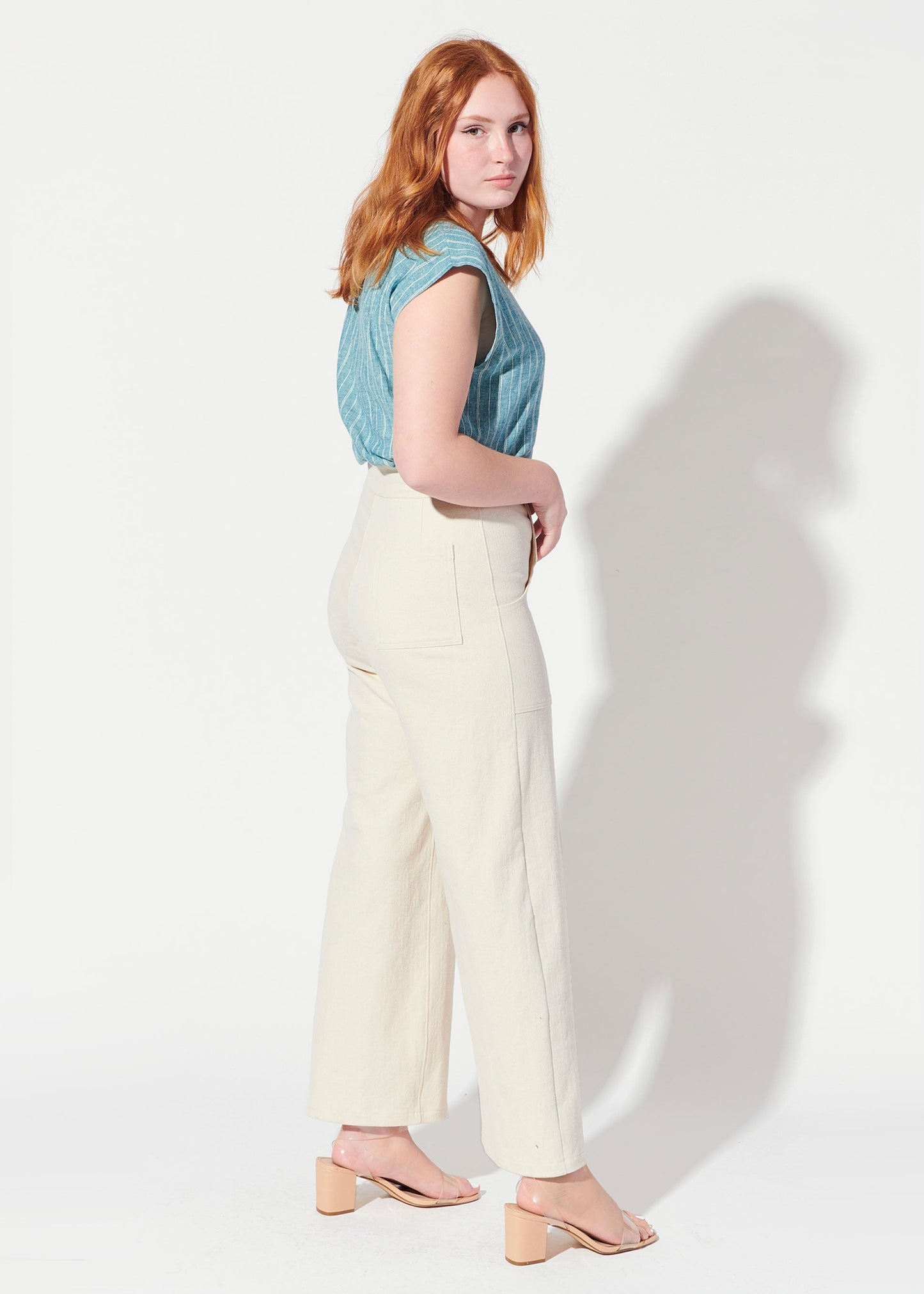 Woman wearing a denim sleeveless top and white pants against a white background