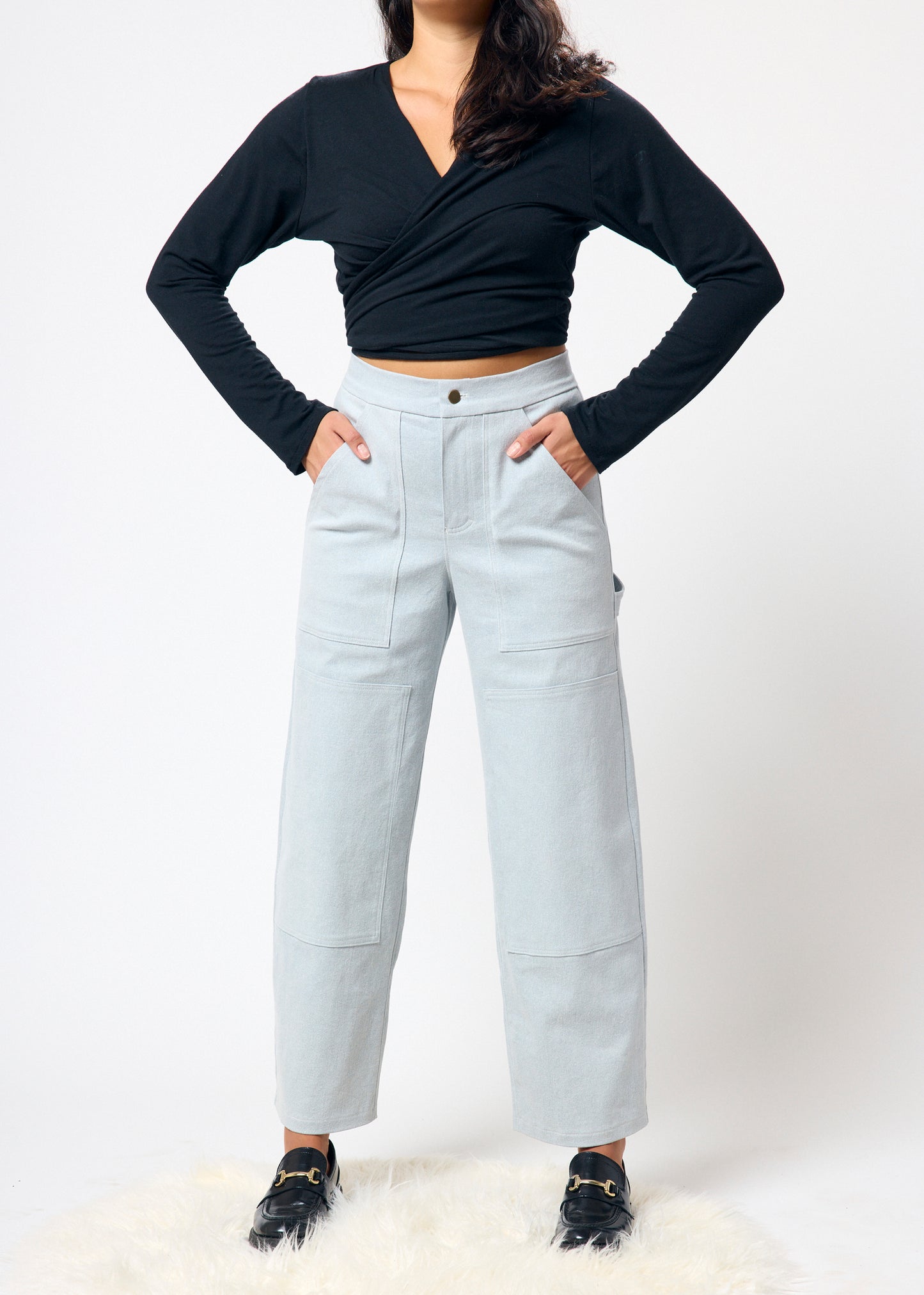 Person wearing a black long-sleeve top and light gray pants on a white background