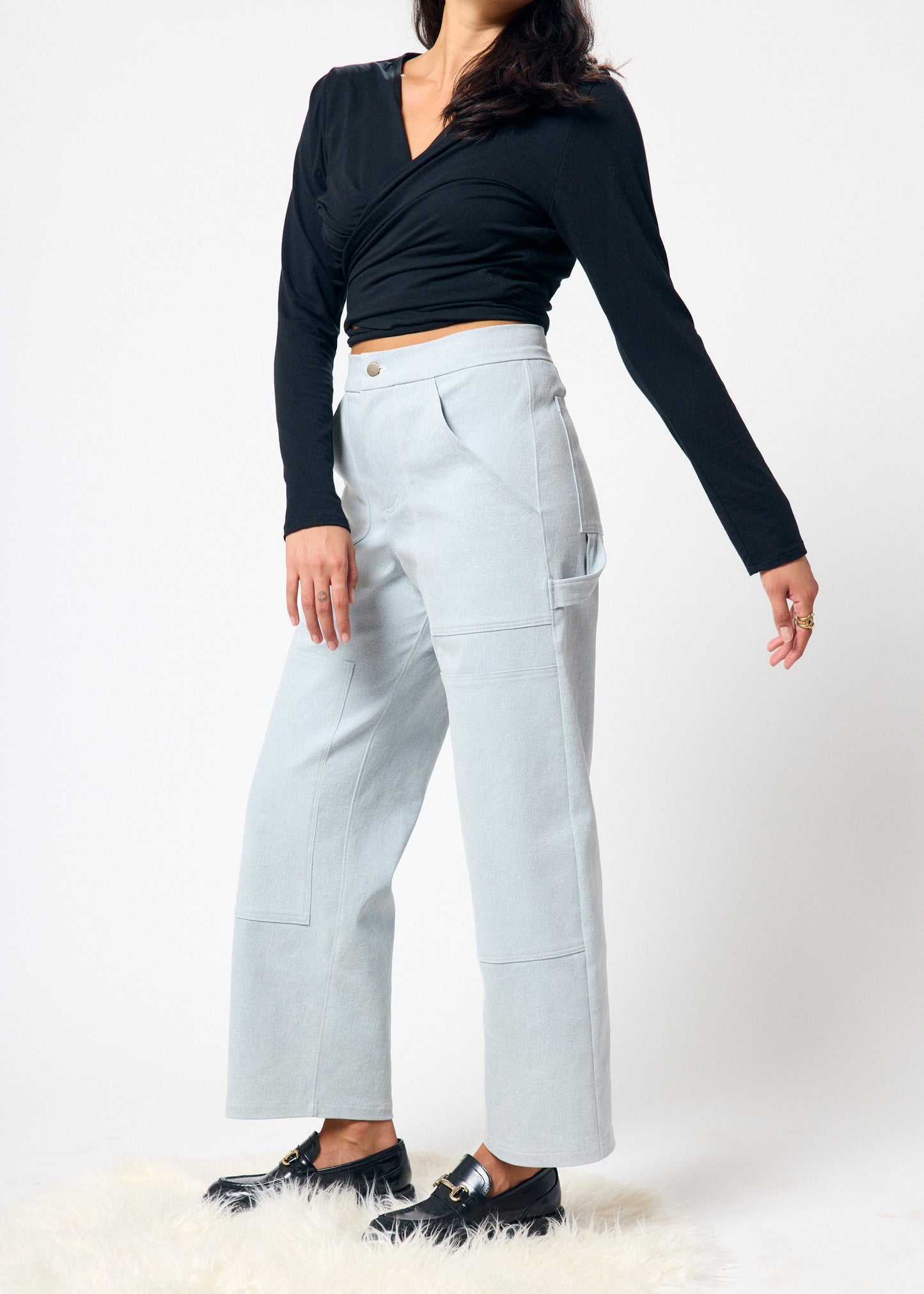 Person wearing a black long-sleeve top and light gray pants on a white background