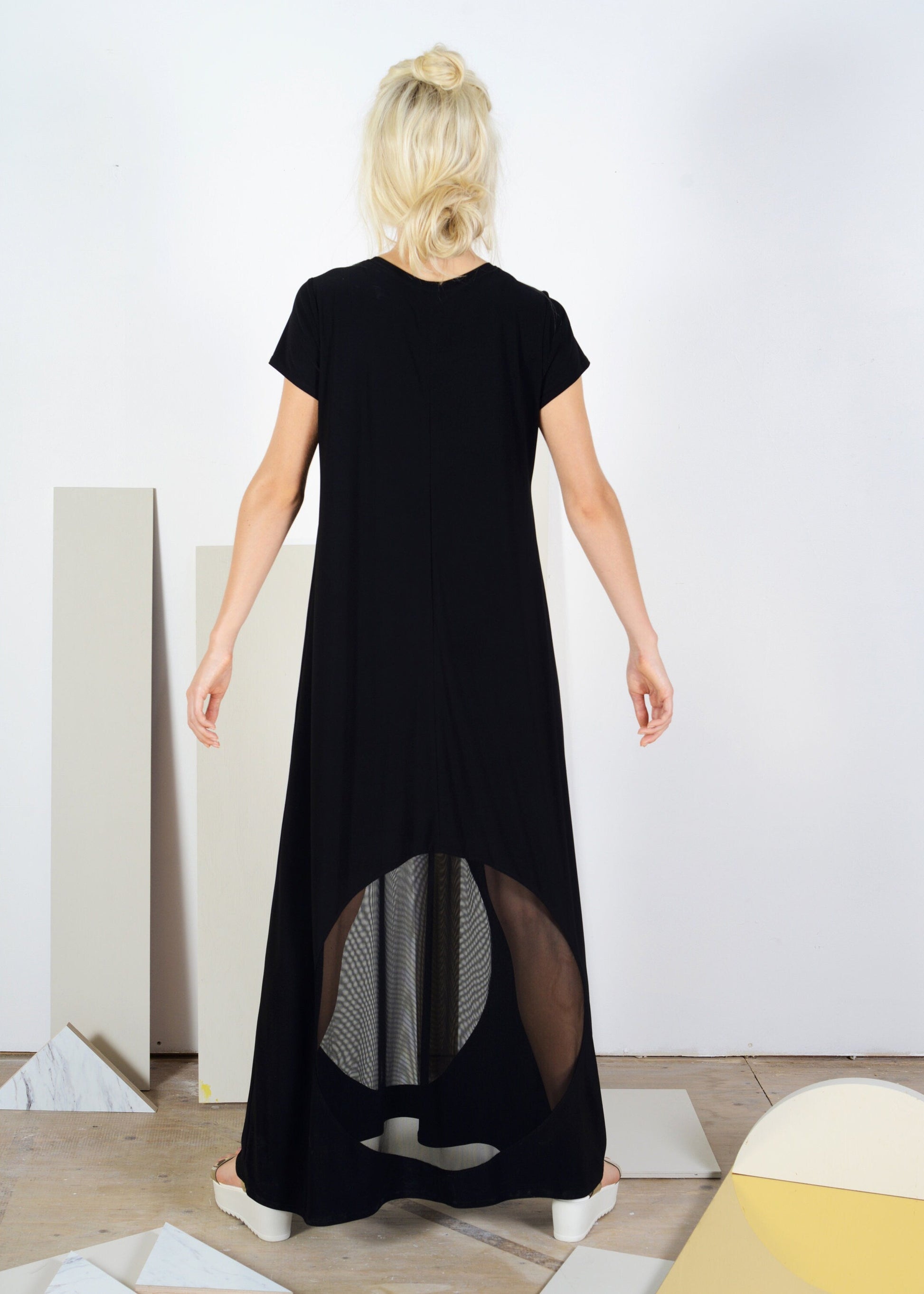 Woman wearing a black dress with a high-low hem in a minimalistic setting.