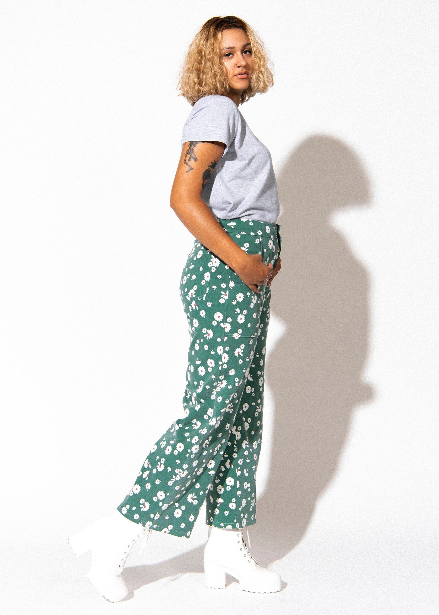 Person wearing a light gray t-shirt and green floral pants on a white background